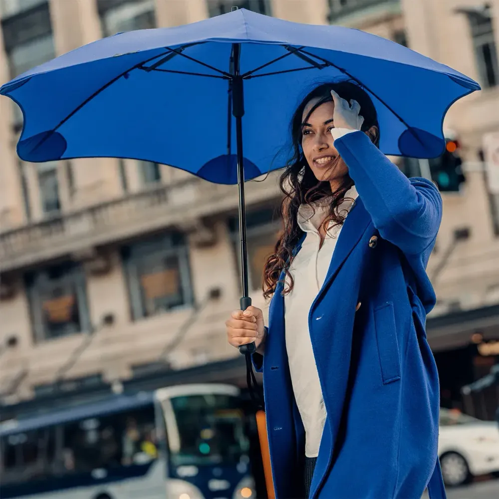 Woman walking with a BLUNT Classic ocean blue umbrella on a city street