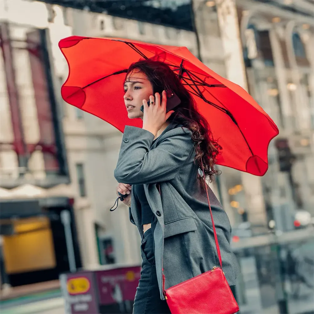 Woman walking in city holding red BLUNT Metro umbrella on rainy day