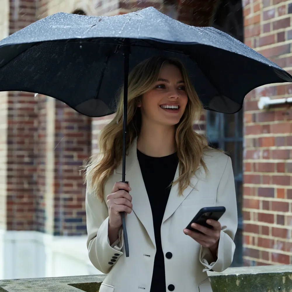 Woman holding BLUNT Metro UV Umbrella in light rain outside brick building