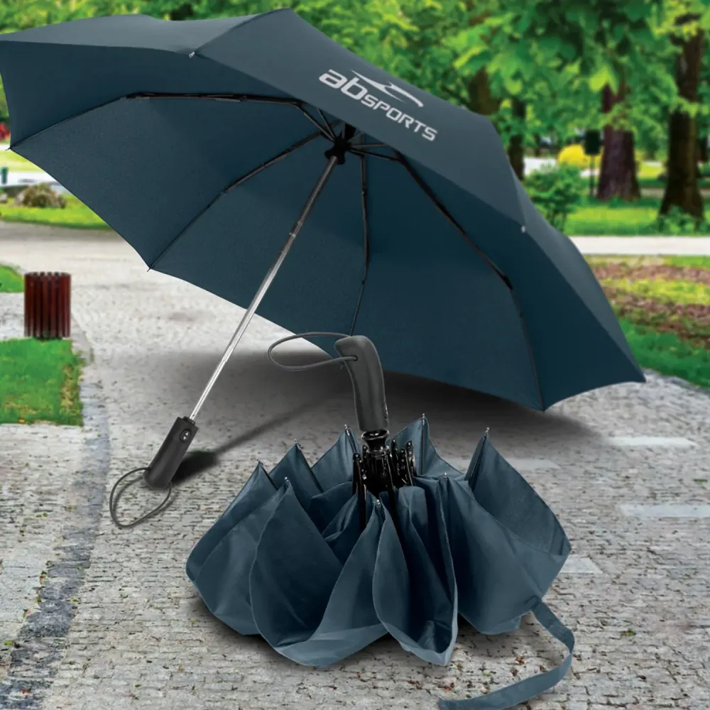 Open Prague Compact umbrella in navy with printed logo on pavement beside folded umbrella
