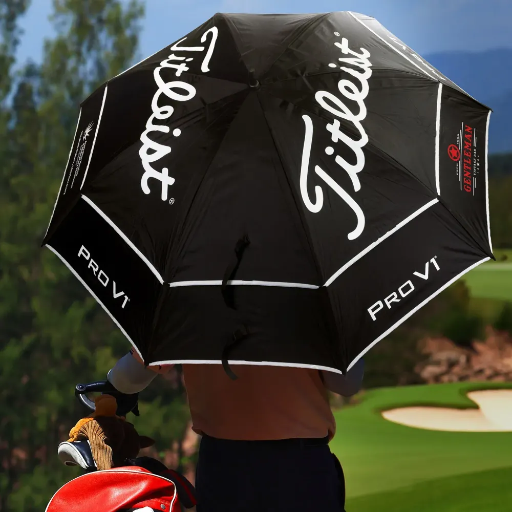 Golfer holding a Titleist Tour Double Canopy Umbrella on a golf course, black canopy with white Titleist and PRO V1 logos