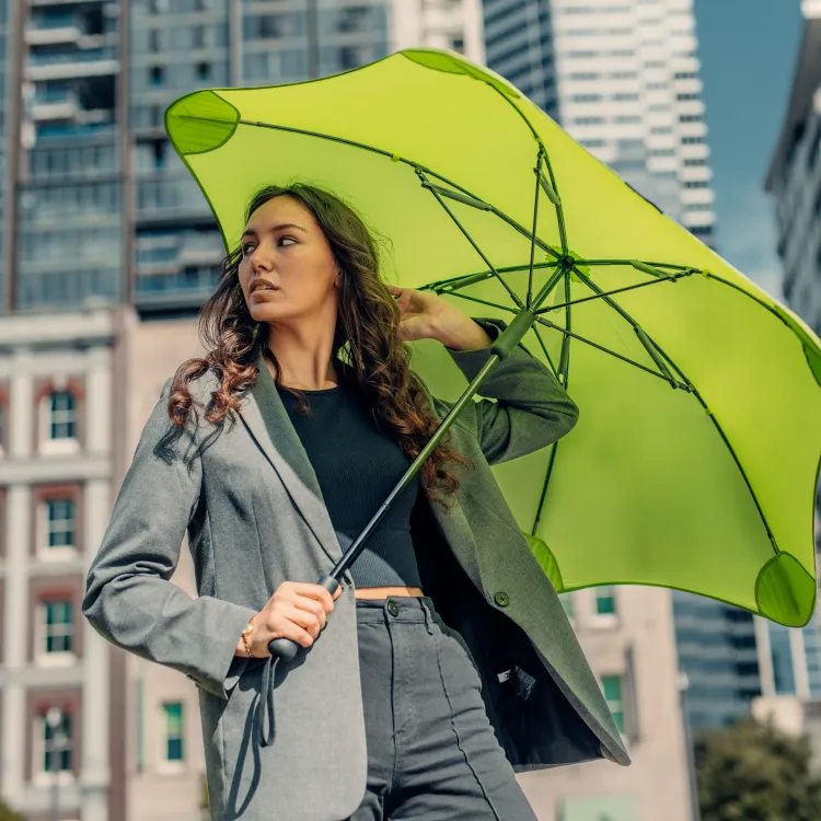 Woman standing by glass wall holding a BLUNT Classic pink umbrella in the rain