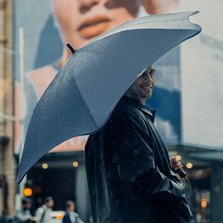 Person smiling under BLUNT Exec umbrella in midnight navy on a rainy city street