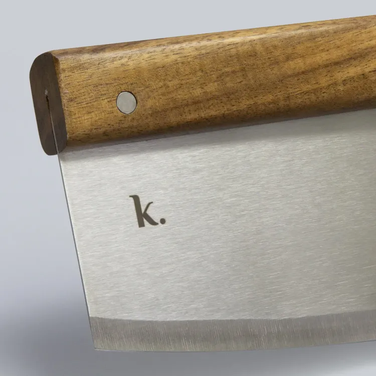 Close-up of stainless steel pizza cutter blade with acacia wood handle and engraved k logo.