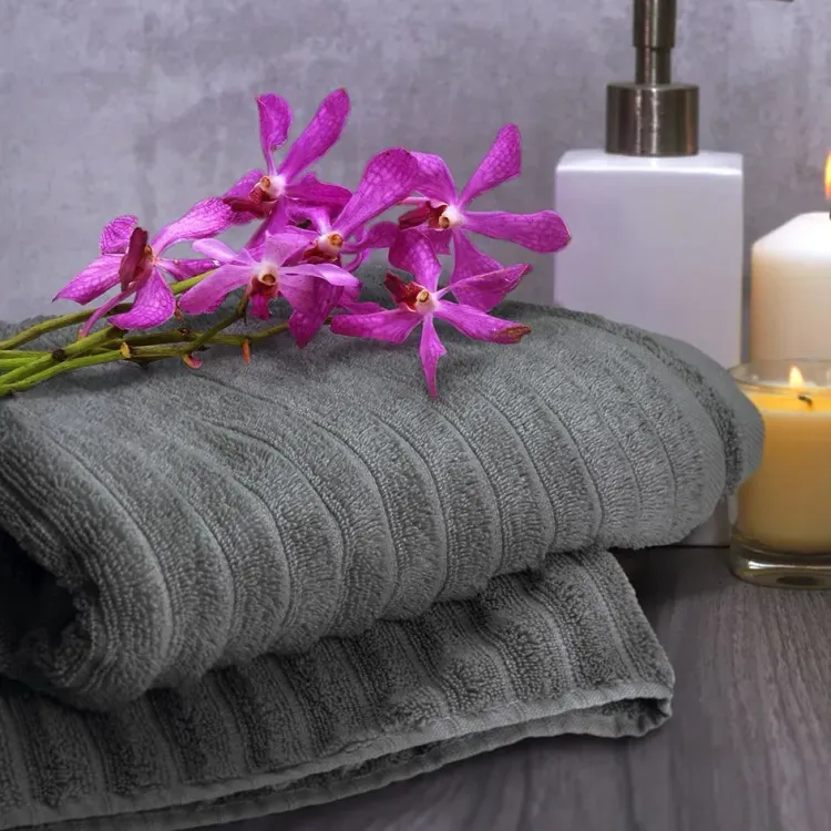 Folded charcoal Palms Luxury Towels with orchid flowers, candle, and dispenser on wooden surface.