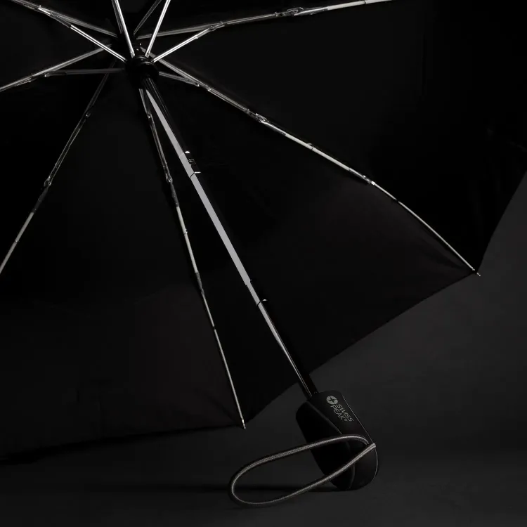 Swiss Peak Traveller Umbrella opened on dark background showing chrome frame, black canopy, and branded handle with wrist strap