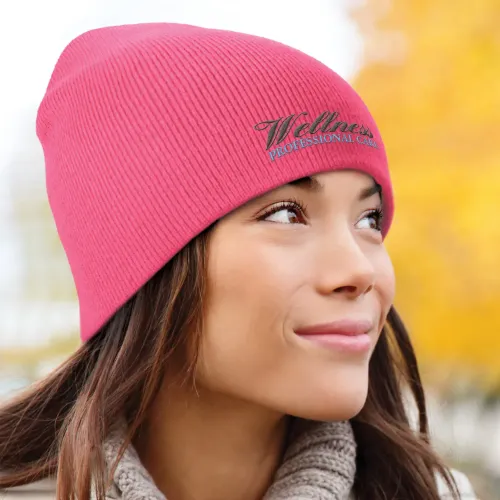 Woman wearing pink beanie embroidered with logo outdoors in autumn.