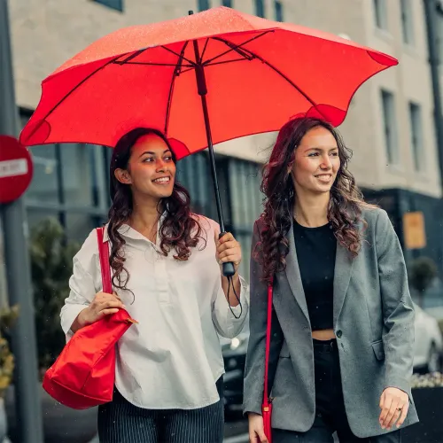 Two women walking in the rain under a BLUNT Classic red umbrella