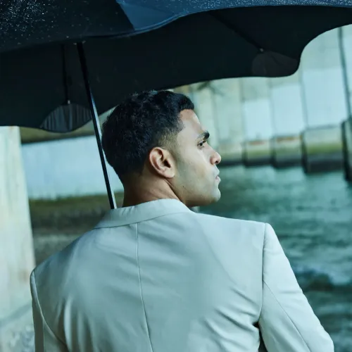 Person standing near waterfront holding BLUNT Exec umbrella in ink black during light rain