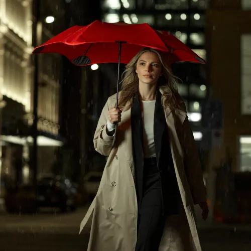 Woman walking at night under red BLUNT Metro umbrella in city rain