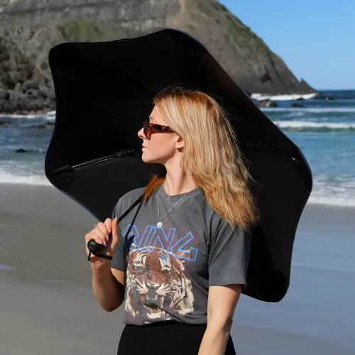Woman holding BLUNT Metro UV Umbrella in black while standing on a sunny beach