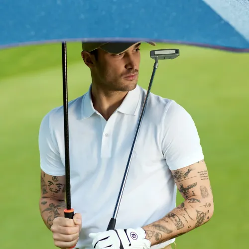 Man standing on golf course holding navy umbrella and golf club while wearing white polo