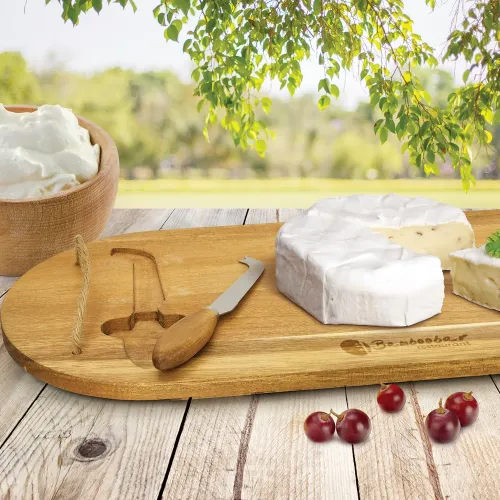 Wooden cheese board with knife, soft cheese, and grapes on outdoor table.