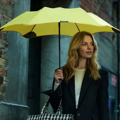 Woman holding yellow umbrella on rainy day in city street.