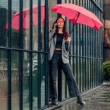 Woman standing by glass wall holding a BLUNT Classic pink umbrella in the rain