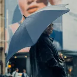 Person smiling under BLUNT Exec umbrella in midnight navy on a rainy city street