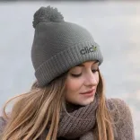 Woman wearing grey Bumble Beanie with embroidered logo and pom-pom outdoors.