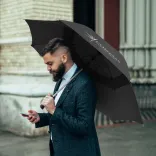 Person holding Hurricane Urban umbrella in black, open profile view with branded panel outdoors