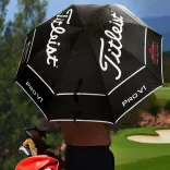 Golfer holding a Titleist Tour Double Canopy Umbrella on a golf course, black canopy with white Titleist and PRO V1 logos